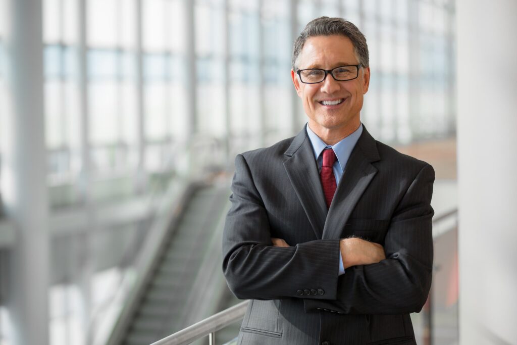 Business man in a suit, arms crossed, smiling.