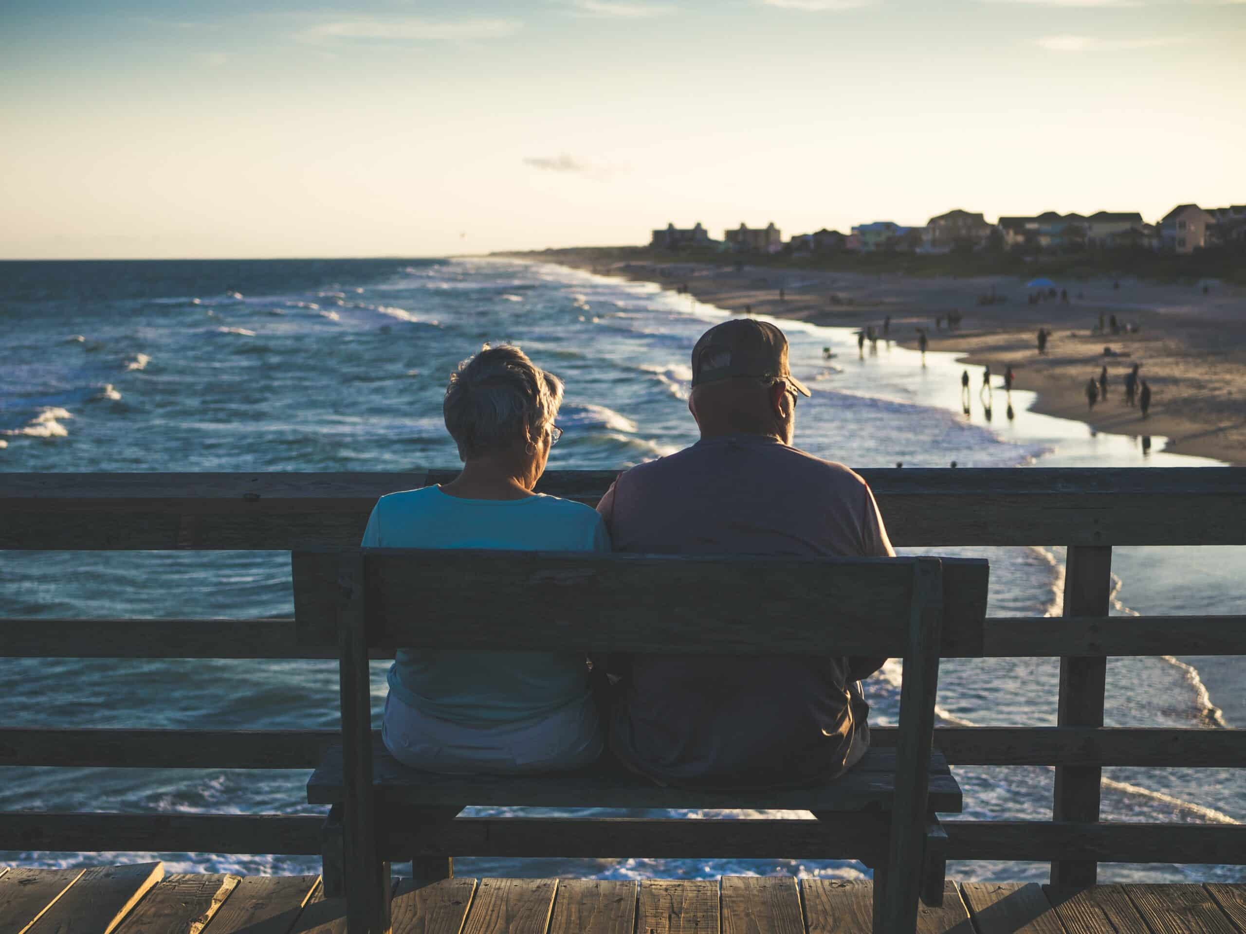 Retired couple, sitting on a bench on a pier, overlooking the ocean waves at almost sunset.