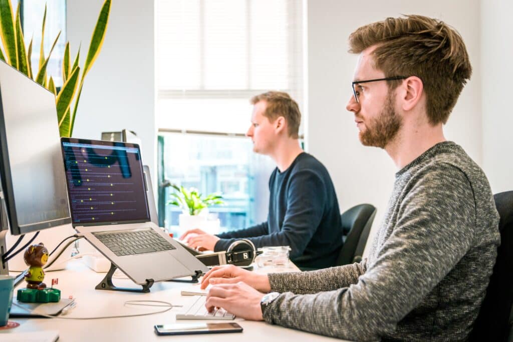 Two men working at a desk, typing on a computer.