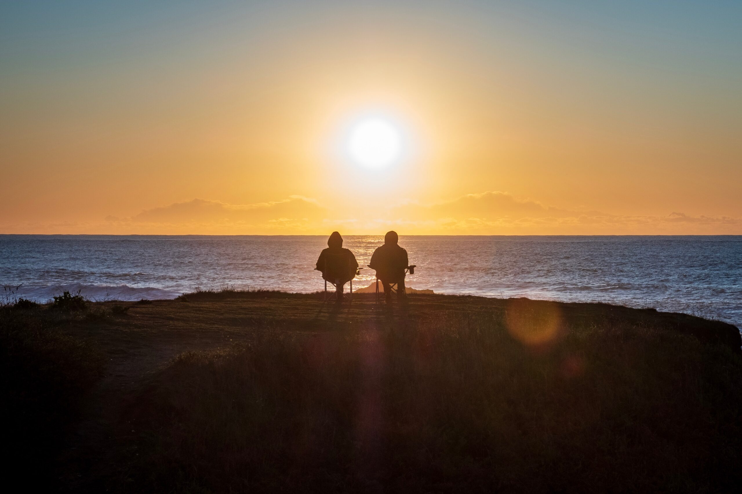 Retired couple sitting on chairs overlooking the ocean at sunset.