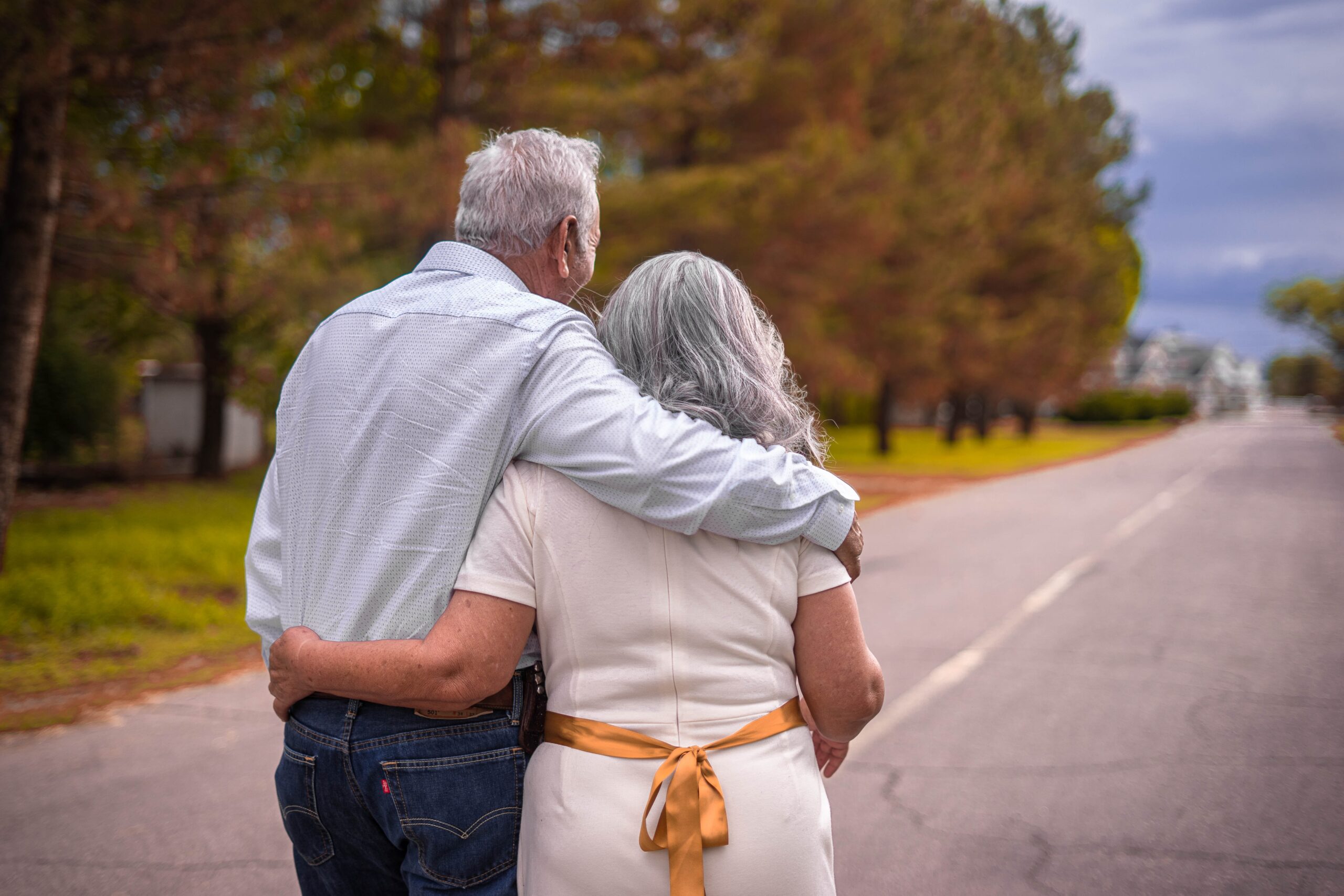 Older couple holding each other as they walk down a road.