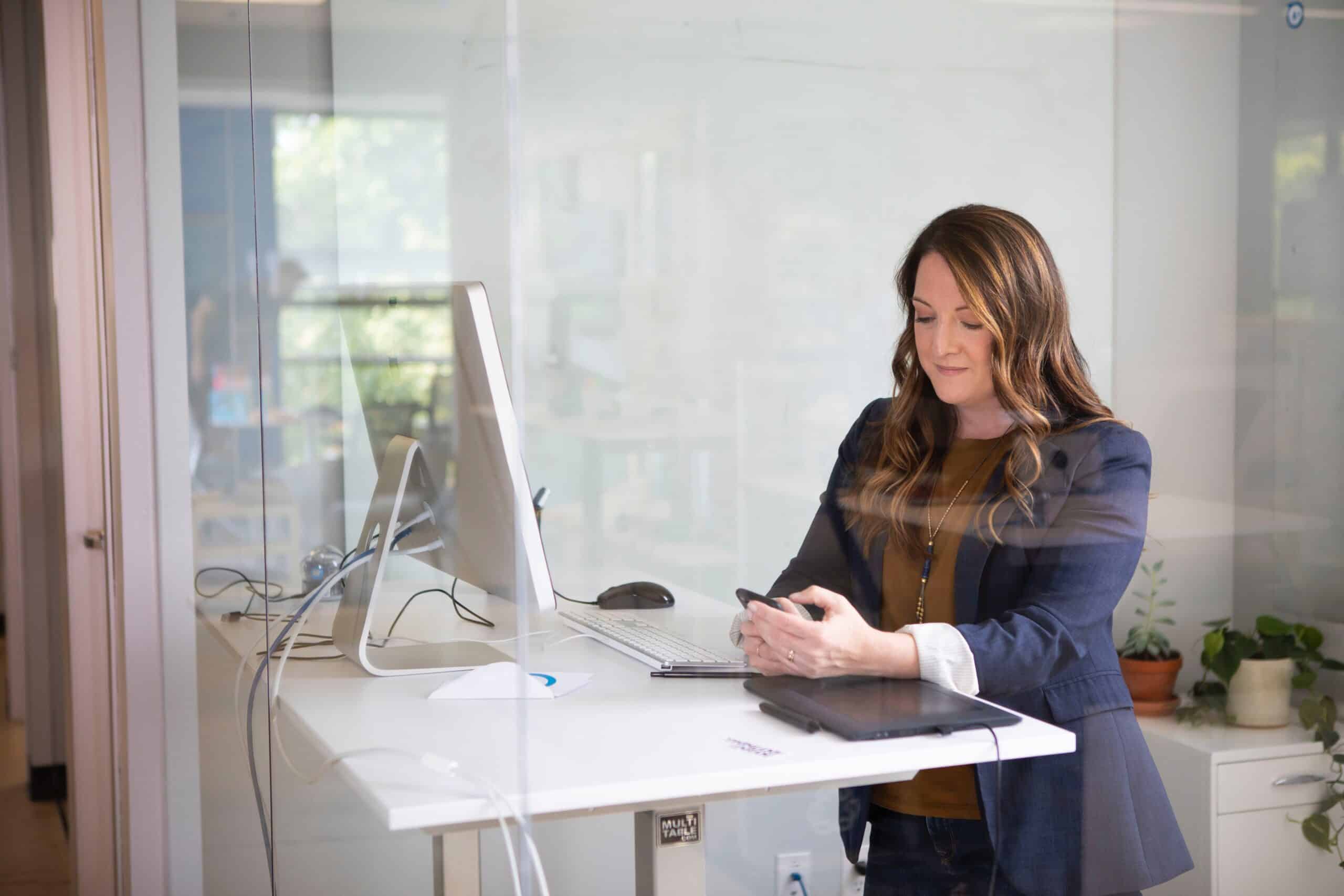 Woman working at a desk and looking at her phone.