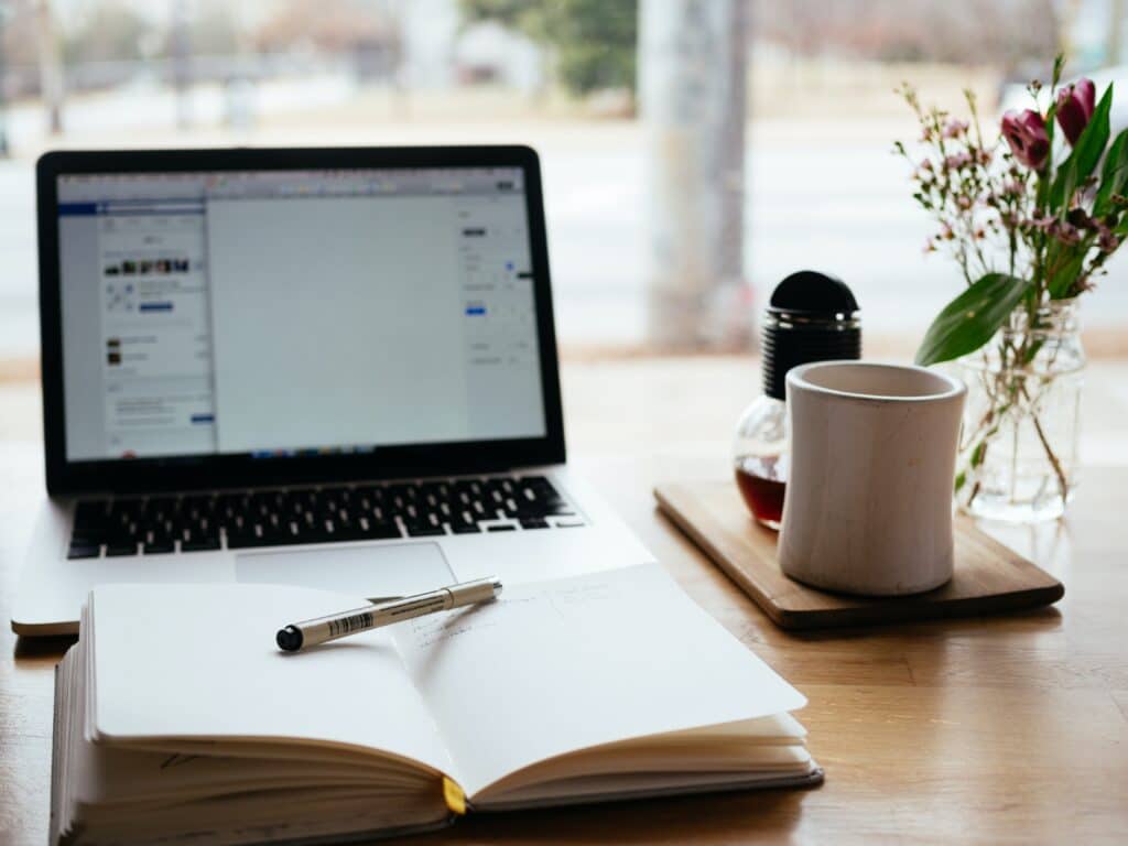 Desk with a laptop, notebook open, coffee.